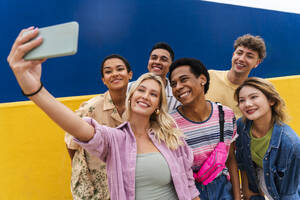 Lachende multiethnische Freunde machen ein Smartphone-Selfie vor einer gelben Wand - OIPF03948