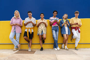 Eine Gruppe von Freunden lehnt an einer gelben Wand und benutzt ihre Smartphones - OIPF03952