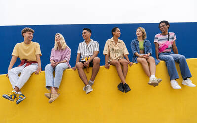 Happy friends with colorful clothing sitting on yellow wall together - OIPF03960