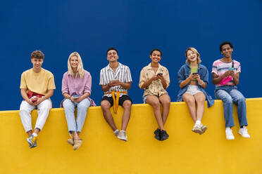 Fröhliche Freunde mit bunter Kleidung sitzen auf Gelb und benutzen ihre Smartphones - OIPF03963