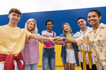 Multiethnische Gruppe junger Freunde, die sich vor einer Wand die Hände reichen - OIPF03998
