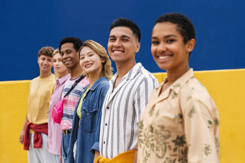 Multi-ethnic group of young friends standing smiling in front of colorful wall - OIPF04006