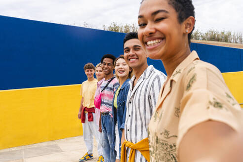 Multi-ethnic group of young friends standing smiling in front of colorful wall - OIPF04009