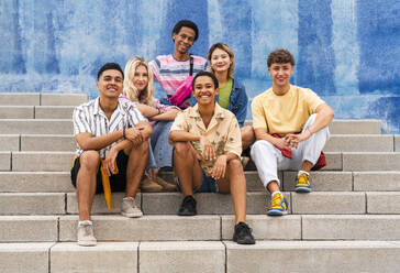 Multiethnische Gruppe junger Menschen, die auf den Stufen vor einer Mauer sitzen - OIPF04010