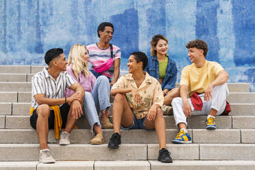 Multiethnische Gruppe junger Menschen, die auf den Stufen vor einer Mauer sitzen - OIPF04011