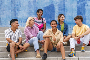 Multiethnische Gruppe junger Menschen, die auf den Stufen vor einer Mauer sitzen - OIPF04013