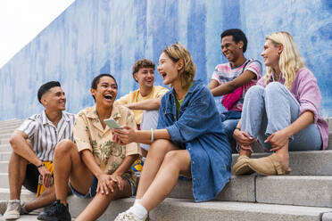 Fröhliche Gruppe junger Leute, die auf den Stufen vor einer Mauer lachen - OIPF04019