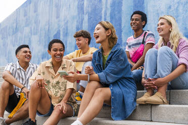 Fröhliche Gruppe junger Leute, die auf den Stufen vor einer Mauer lachen - OIPF04020