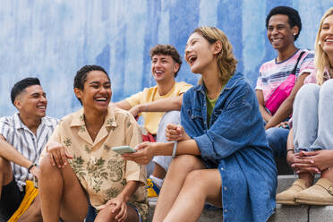 Fröhliche Gruppe junger Leute, die auf den Stufen vor einer Mauer lachen - OIPF04021