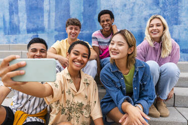 Fröhliche Gruppe junger Leute, die ein Selfie auf einer Treppe vor einer Mauer machen - OIPF04022