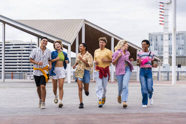 Unterschiedliche Gruppe junger Freunde mit farbenfroher Kleidung, die gemeinsam Spaß beim Laufen im Freien haben - OIPF04041