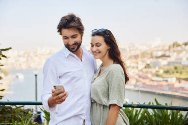 Glückliches junges Paar benutzt Smartphone an einem sonnigen Tag - BSZF02624