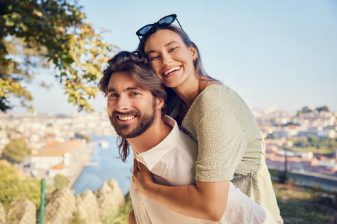 Smiling man giving piggyback ride to woman - BSZF02628