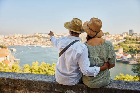 Young man gesturing with woman sitting in front of Porto city in Portugal - BSZF02632