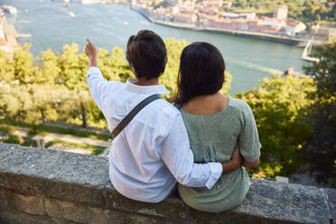 Junger Mann gestikuliert mit einer Frau, die vor dem Fluss Douro sitzt, Stadt Porto in Portugal - BSZF02633