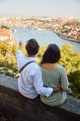 Mann gestikuliert mit einer Frau, die vor dem Fluss Douro sitzt, Stadt Porto in Portugal - BSZF02634