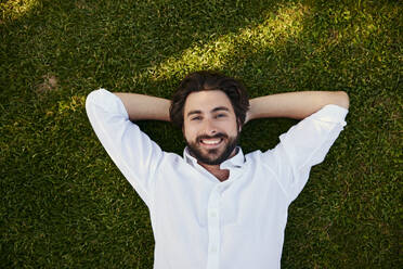 Smiling young man lying on grass - BSZF02638