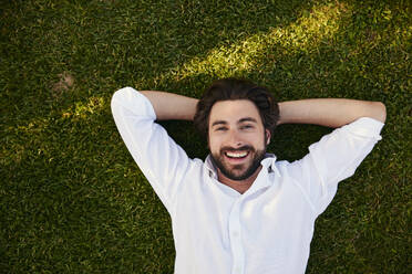 Happy young man lying on grass - BSZF02639