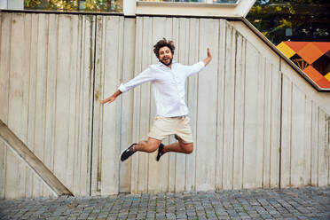 Happy young man jumping in front of wall - BSZF02651