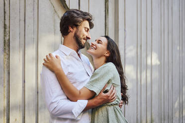 Smiling couple embracing each other in front of wall - BSZF02655