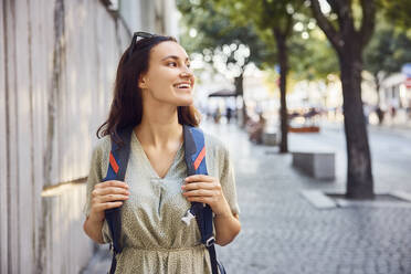 Happy young woman walking with backpack on footpath - BSZF02657