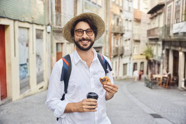 Lächelnder junger Mann mit Kaffeetasse und traditioneller Süßspeise Pastel de Nata - BSZF02660