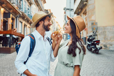 Happy couple holding traditional dessert near buildings - BSZF02666