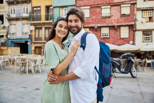 Lächelndes junges Paar steht zusammen vor einem Gebäude - BSZF02672