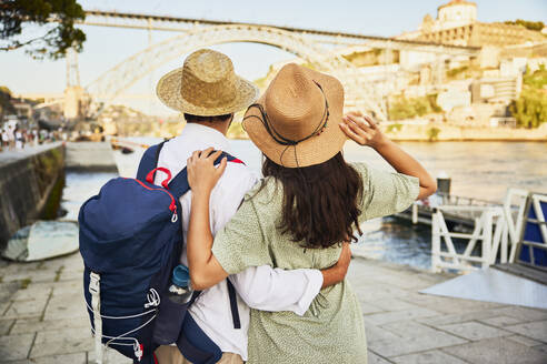 Young couple wearing hat and standing in front of Dom Luis bridge at Porto, Portugal - BSZF02675