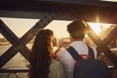 Junges Paar beim Fotografieren mit dem Smartphone bei Sonnenuntergang - BSZF02685