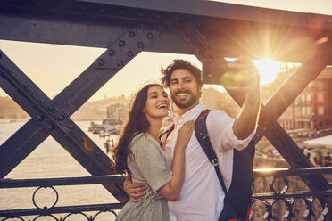 Smiling couple taking selfie through smart phone at Dom Luis bridge, Porto, Portugal - BSZF02686