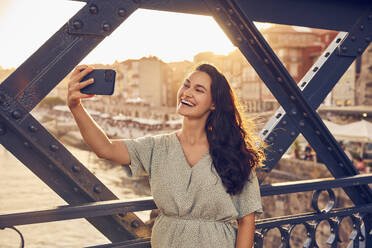 Glückliche junge Frau, die ein Selfie mit ihrem Handy an der Dom-Luis-Brücke macht, Porto, Portugal - BSZF02689