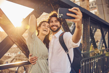 Cheerful couple taking selfie through smart phone at Dom Luis bridge, Porto, Portugal - BSZF02691