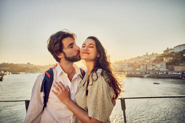 Happy man kissing woman in front of Douro river at Porto, Portugal - BSZF02699