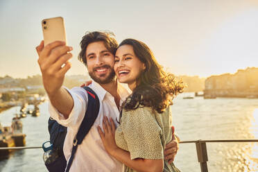 Glückliches Paar nimmt Selfie durch Smartphone vor Douro Fluss bei Sonnenuntergang - BSZF02701