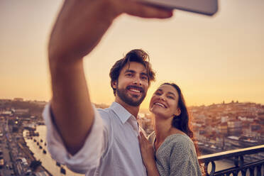 Glückliches Paar nimmt Selfie durch Smartphone vor Porto Stadt bei Sonnenuntergang, Portugal - BSZF02719