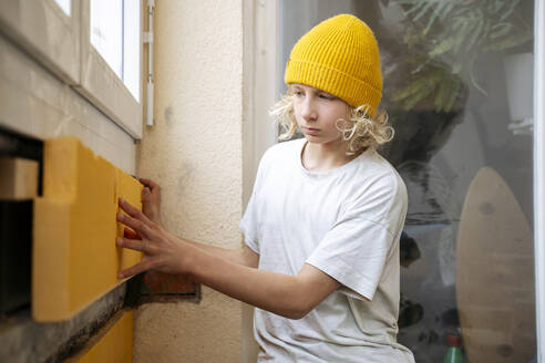 Boy installing insulation on wall in room under renovation - NJAF00807