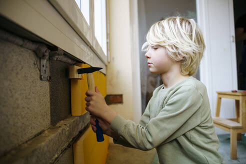 Boy hammering wooden piece on wall in room under renovation - NJAF00810