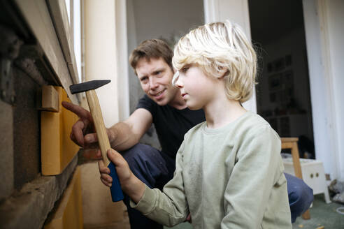 Father teaching boy to install insulation on wall at home - NJAF00811