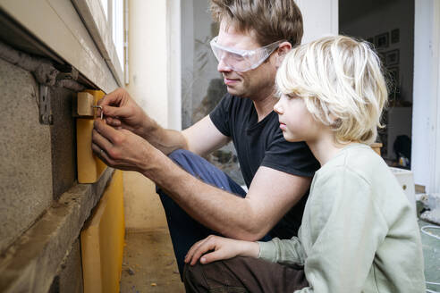 Mature father teaching son to install insulation at home - NJAF00818