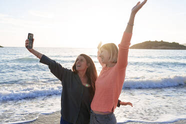 Carefree friends with arms outstretched taking selfie at beach - JOSEF23658