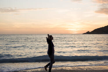 Carefree woman with arms outstretched walking at sunset beach - JOSEF23676