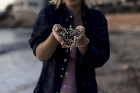 Woman throwing pebbles with hands cupped at sunset beach - JOSEF23680