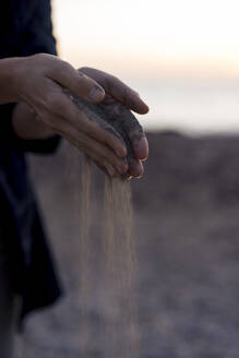 Frau wirft Sand mit gefalteten Händen am Strand bei Sonnenuntergang - JOSEF23681