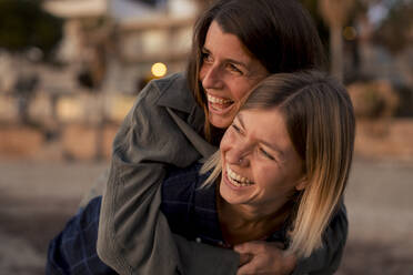 Happy woman piggybacking friend at sunset beach - JOSEF23686