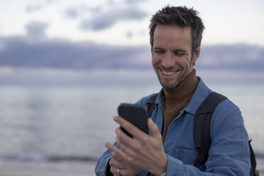 Glücklicher Mann benutzt Smartphone am Strand - JOSEF23691