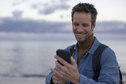 Happy man using smart phone at beach - JOSEF23691