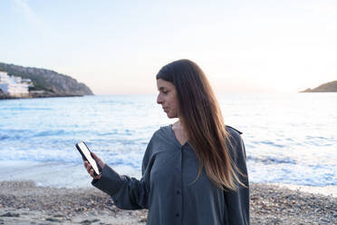 Frau benutzt Smartphone bei Sonnenuntergang am Strand - JOSEF23729