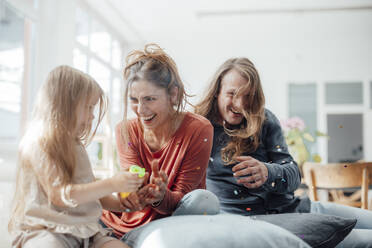 Cheerful parents with daughter holding party popper at home - JOSEF23736