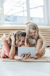 Lächelndes Mädchen mit Mutter, die zu Hause einen Tablet-PC benutzt - JOSEF23747